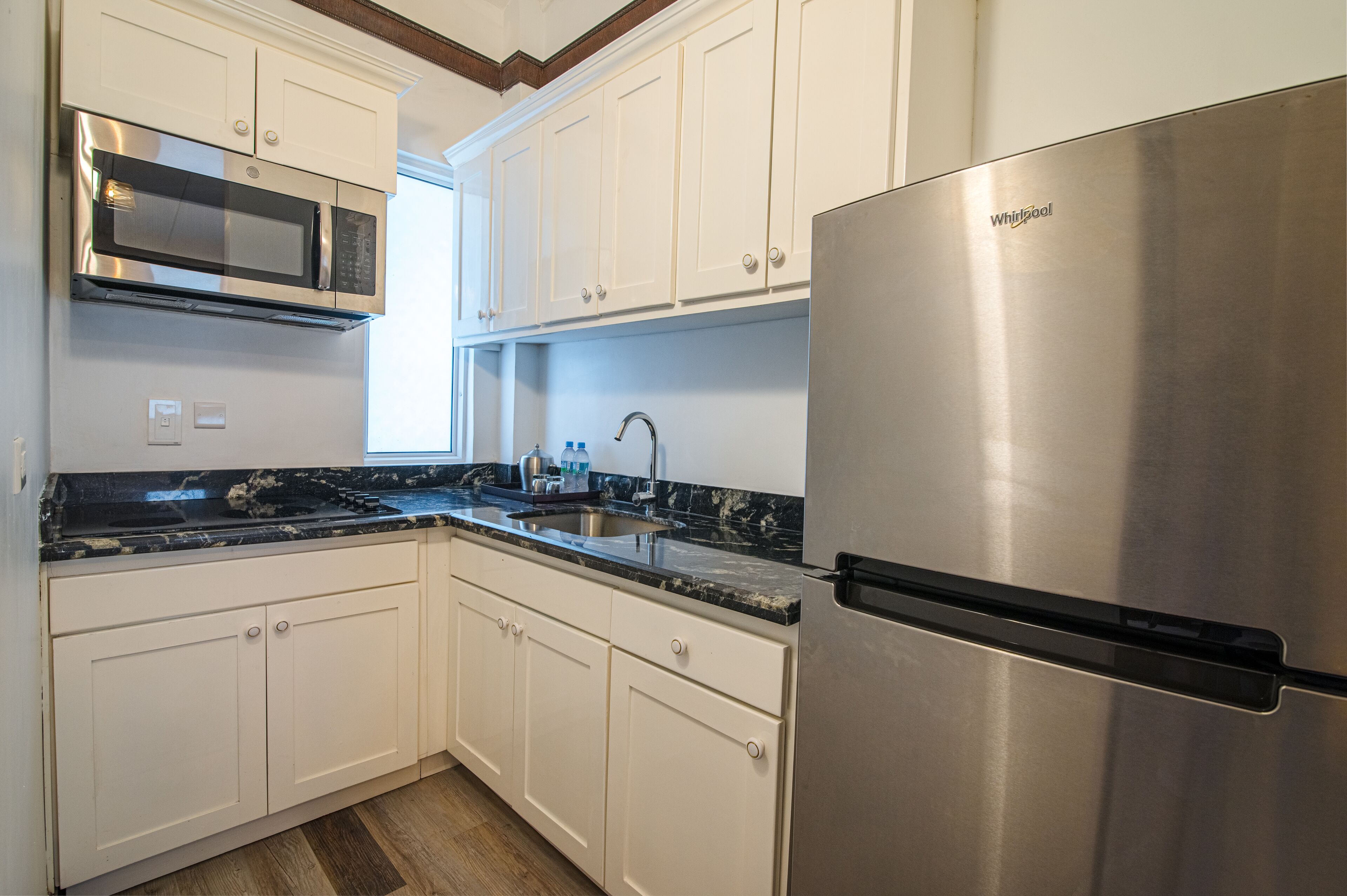 A kitchen with white cabinets, a stainless steel refrigerator, a microwave, and a granite countertop.