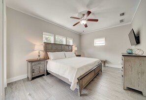 Ein Schlafzimmer mit einem Bett, Nachttischen, einem Deckenventilator, einem Schminktisch und einem Fernseher an der Wand.