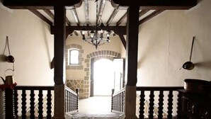 Un couloir avec un mur en pierre, une rambarde en bois et un lustre.