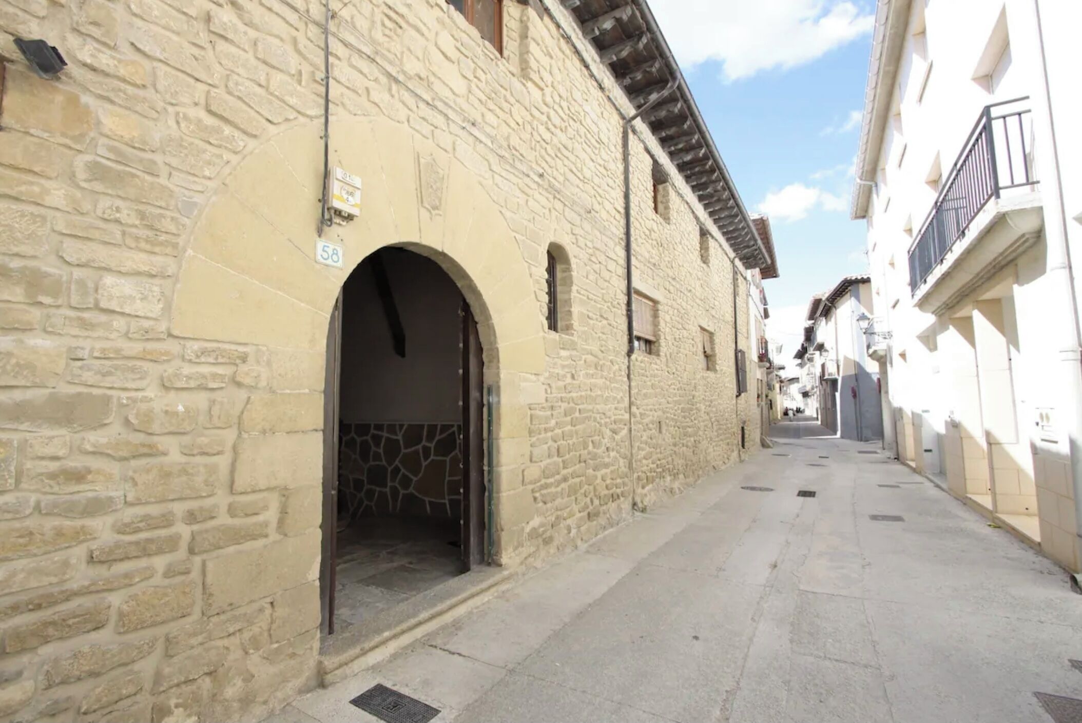 Una calle estrecha con edificios de piedra, uno con el número '58' visible y una entrada en arco.
