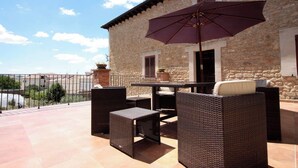 Une terrasse extérieure aménagée avec des meubles en osier et un grand parasol, située devant un bâtiment en pierre et offrant une vue sur le paysage.
