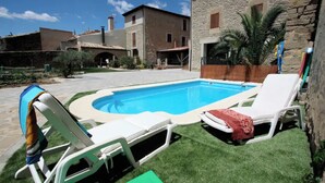 Une piscine avec des chaises longues et, en arrière-plan, un bâtiment en pierre.
