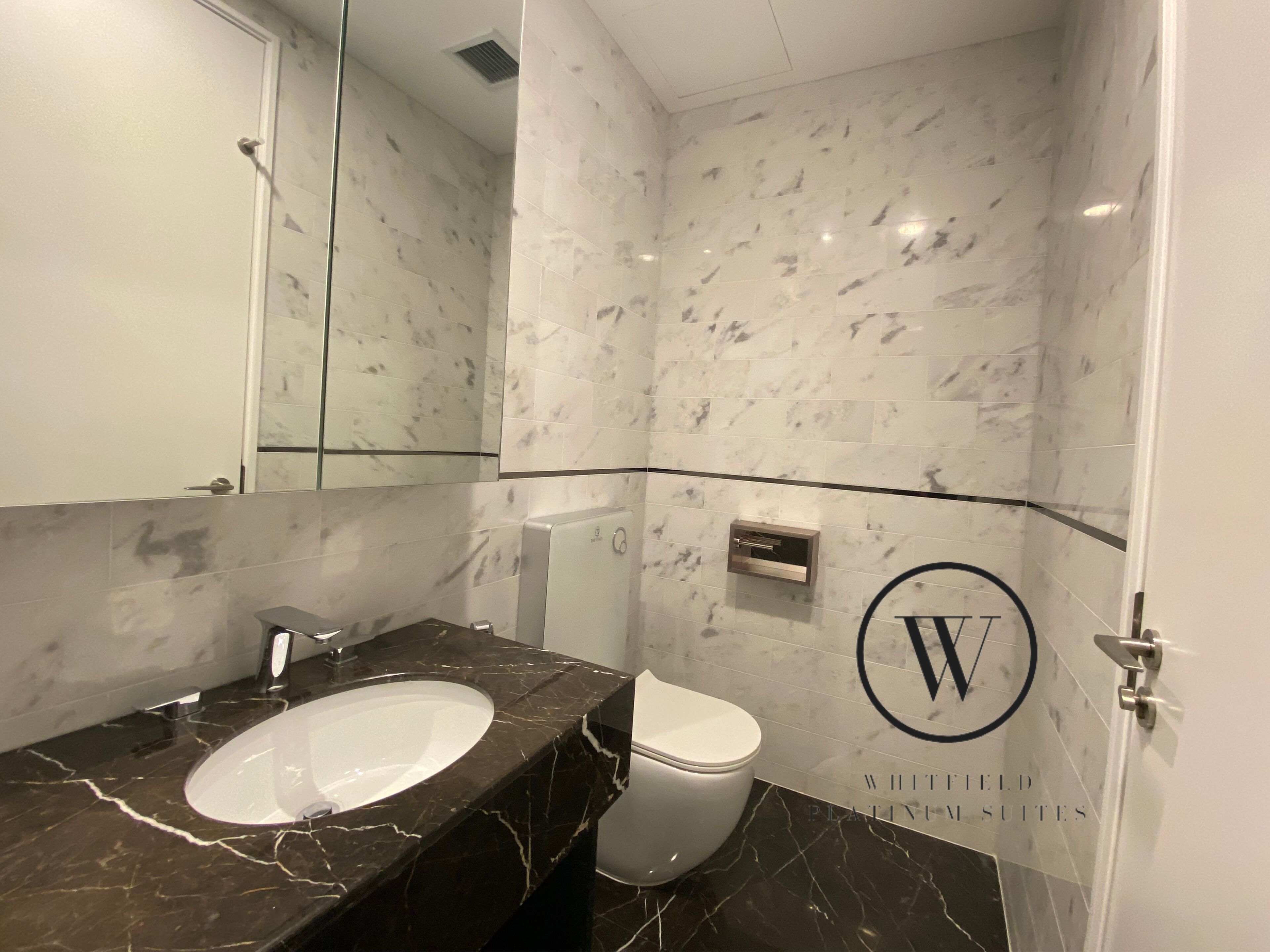 A bathroom with a marble sink, toilet, and a large mirror.