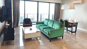 A modern living room with a green sofa, a coffee table, a TV, and a dining area with chairs and a table. - Victory suites  (Kuala Lumpur)