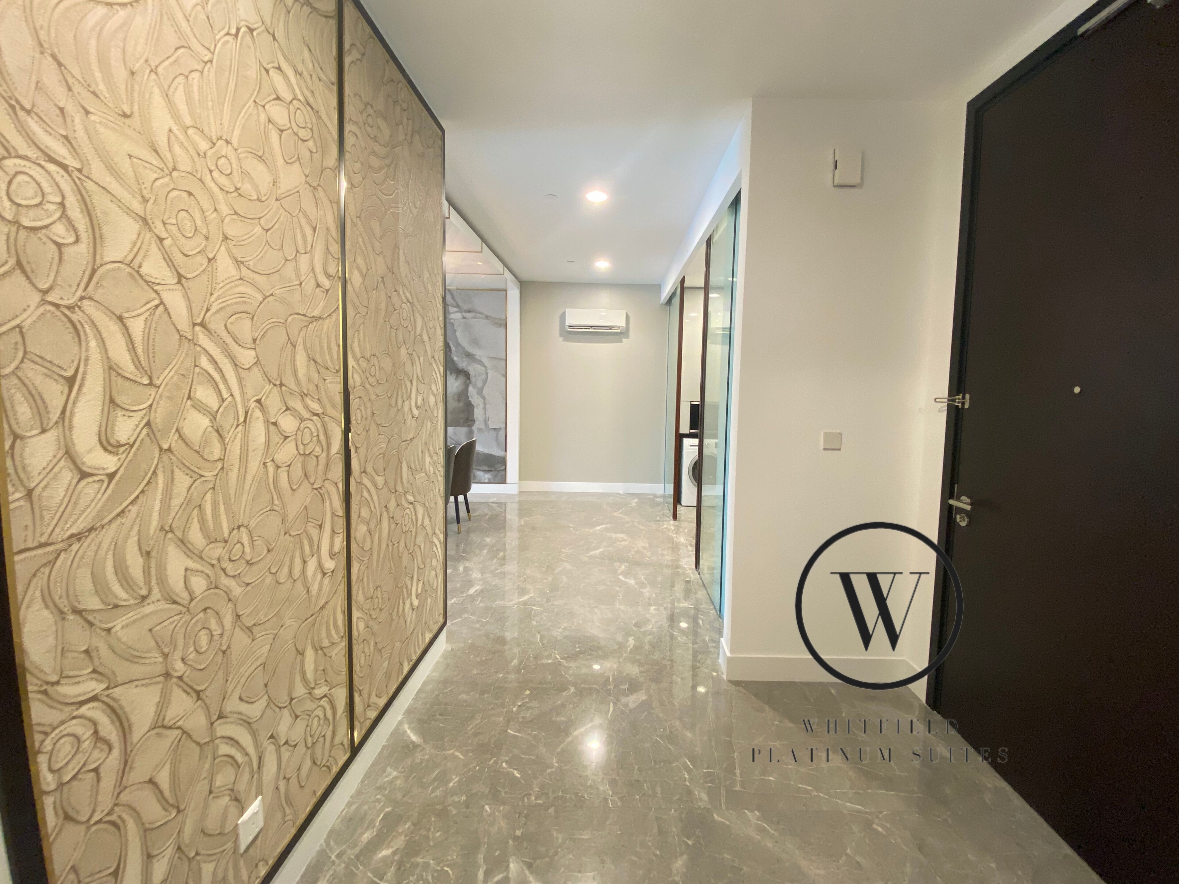 A hallway with a marble floor, a decorative panel with floral patterns, and a door with a 'W' logo.
