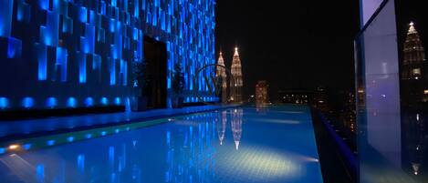 A modern building with a reflective pool and a view of the Petronas Towers at night.