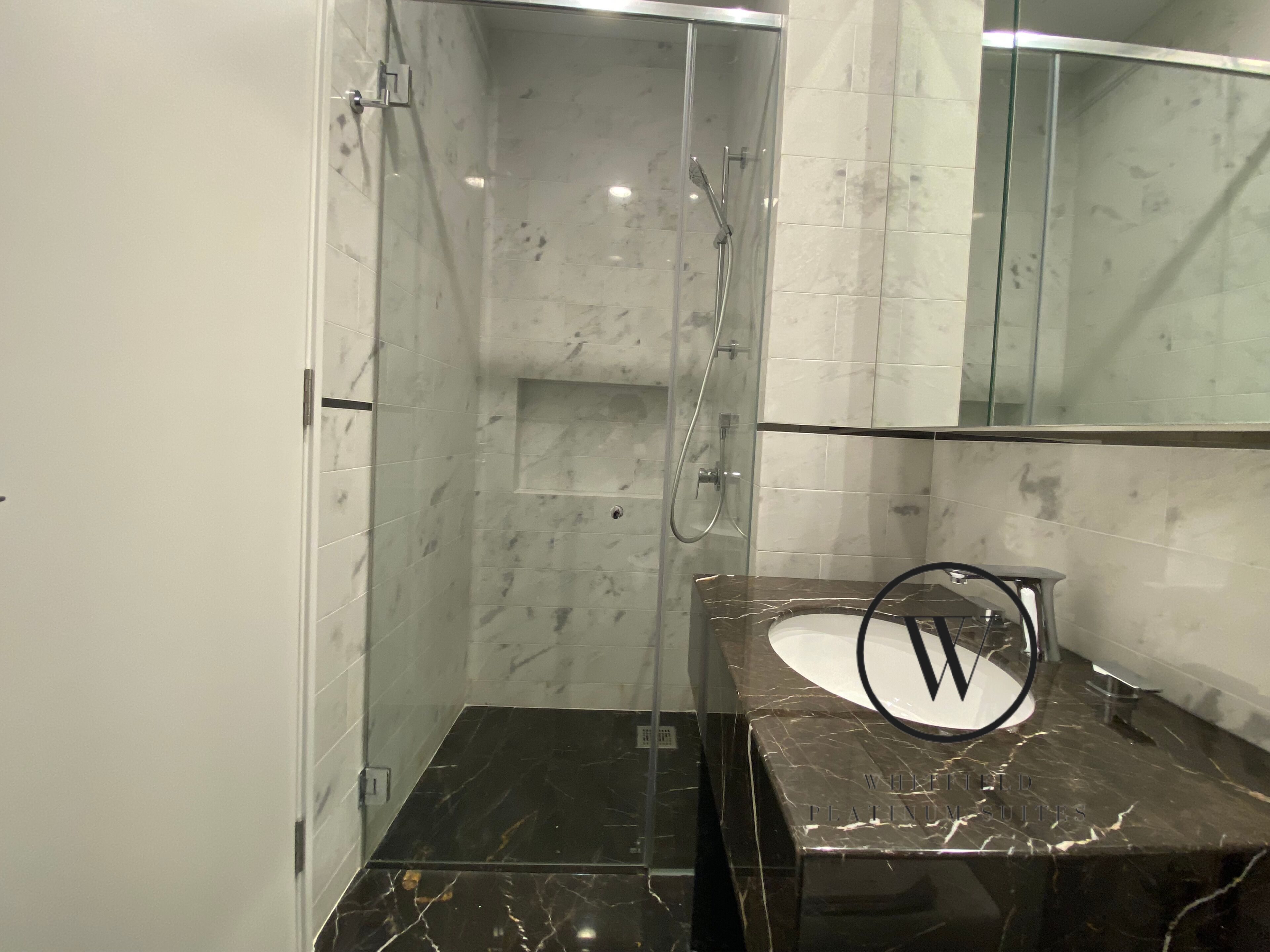 A modern bathroom with a glass-enclosed shower, a marble vanity, and a large mirror.