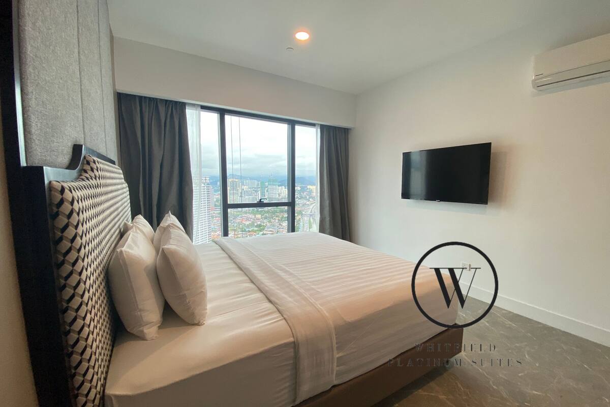 A modern hotel room with a large bed, a flat-screen TV, and a city view.
