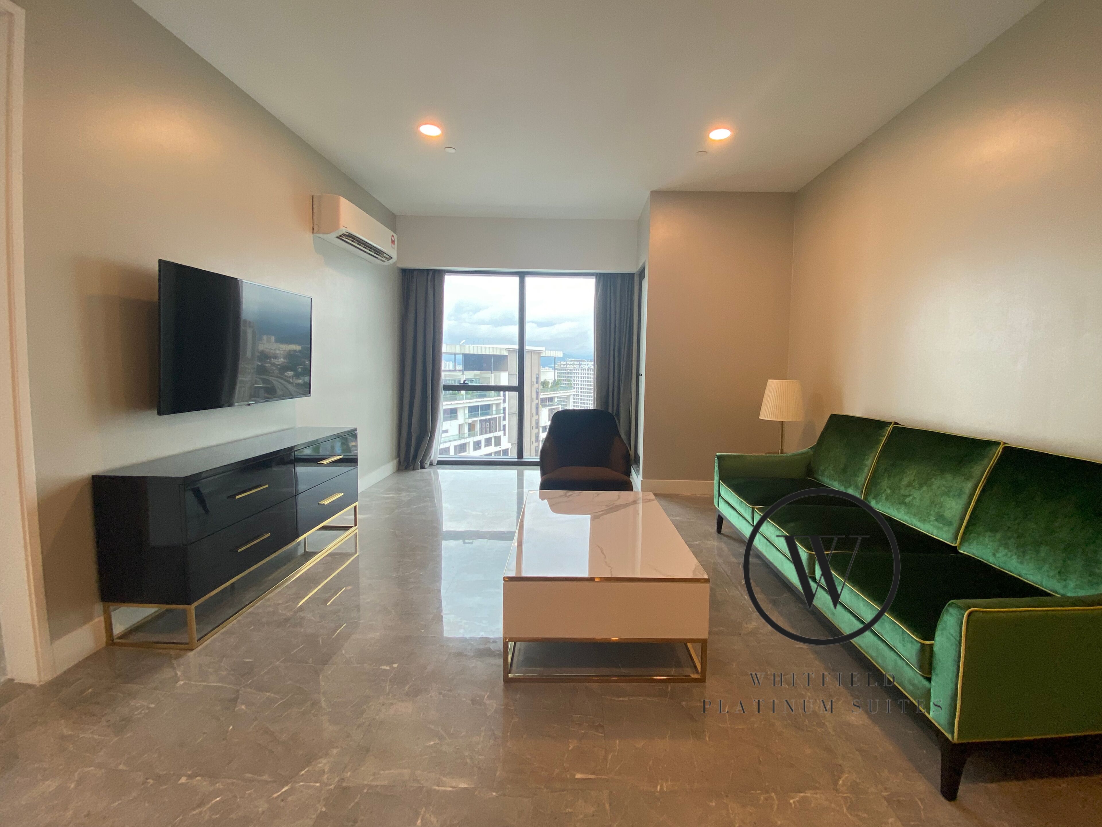 Una sala de estar moderna con un televisor de pantalla plana, un sofá verde, una mesa de centro y vistas de la ciudad a través de ventanas amplias.
