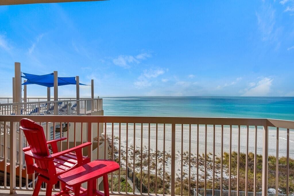 Un balcon avec vue sur la plage, des chaises rouges et un auvent bleu.