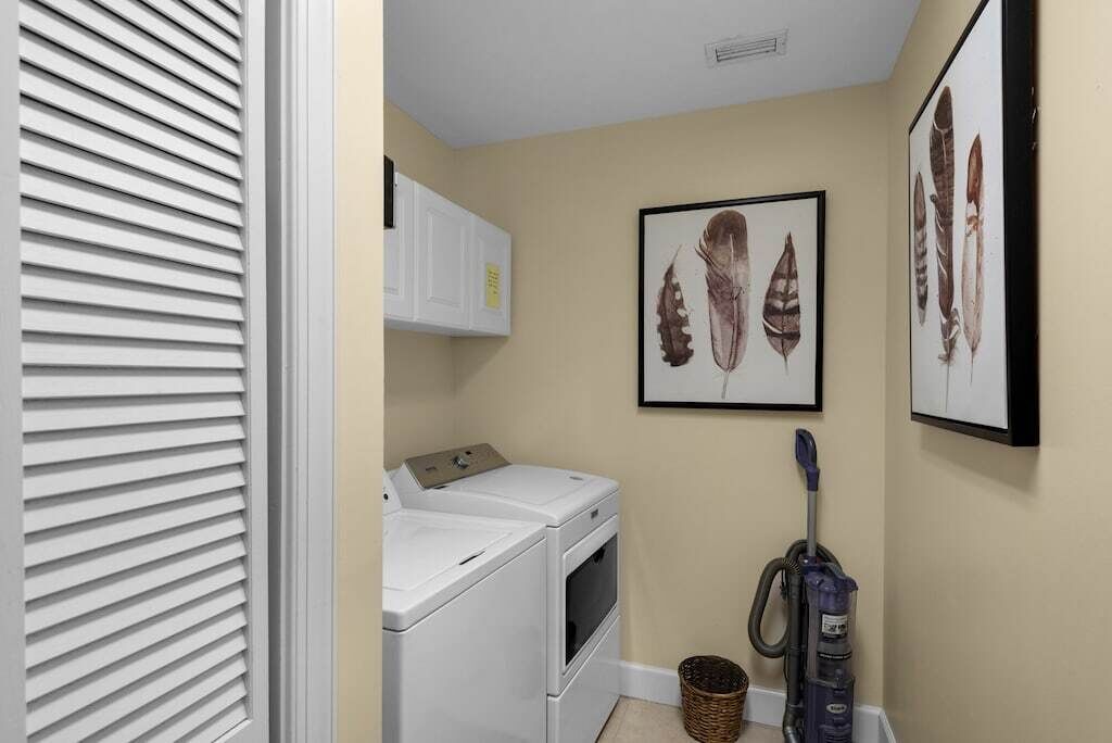 A laundry room with a washer and dryer, a vacuum cleaner, and framed feather art on the wall.