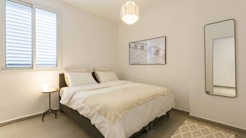 A bedroom with a bed, a bedside table with a lamp, a framed picture on the wall, and a mirror.