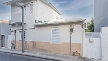 A two-story building with a balcony, a visible air conditioning unit, and a gated entrance.