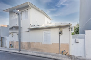 A two-story building with a balcony, a visible air conditioning unit, and a gated entrance.