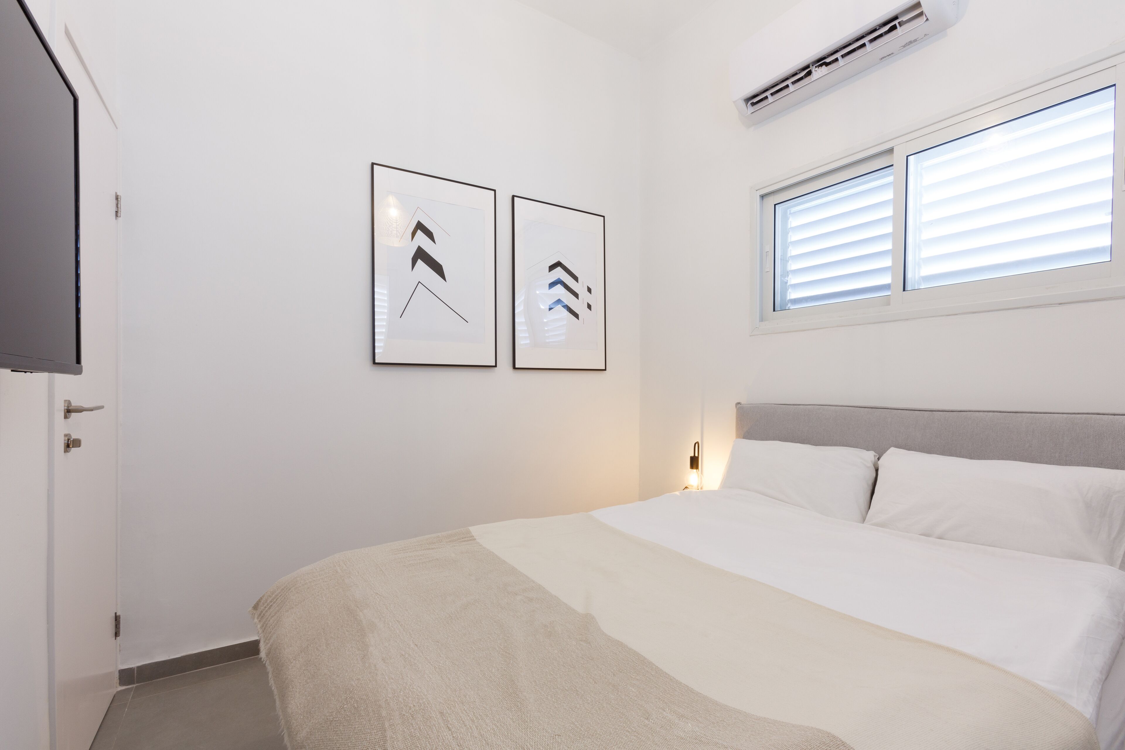 A bedroom with a bed, a TV, and two framed pictures on the wall.