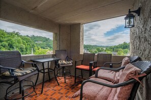 A balcony with wicker furniture, a table, and a view of a green landscape.