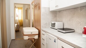 Una cocina compacta equipada con microondas, tostadora y hervidor. Una maleta está sobre un taburete cerca de la puerta.