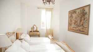 Habitación de hotel con dos camas, un tocador con espejo, una araña y un cuadro grande en la pared.