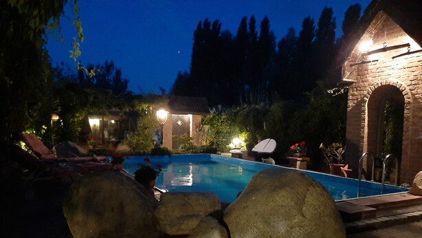 Un espace extérieur avec piscine, aménagé pour la nuit, comprenant un mur en pierre, des chaises longues et une petite construction en briques.