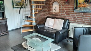 Un salon moderne avec un escalier en colimaçon, un canapé en cuir, une table basse en verre et un mur de briques orné d’œuvres d’art.