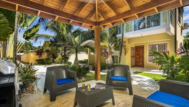 Une terrasse extérieure aménagée avec des meubles en osier, un barbecue et des plantes tropicales.
