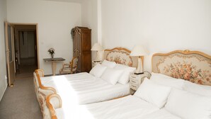 Ett hotellrum med en dubbelsäng, ett träbord vid sängen med lampor, en spegel och en dörr som leder till ett annat rum.