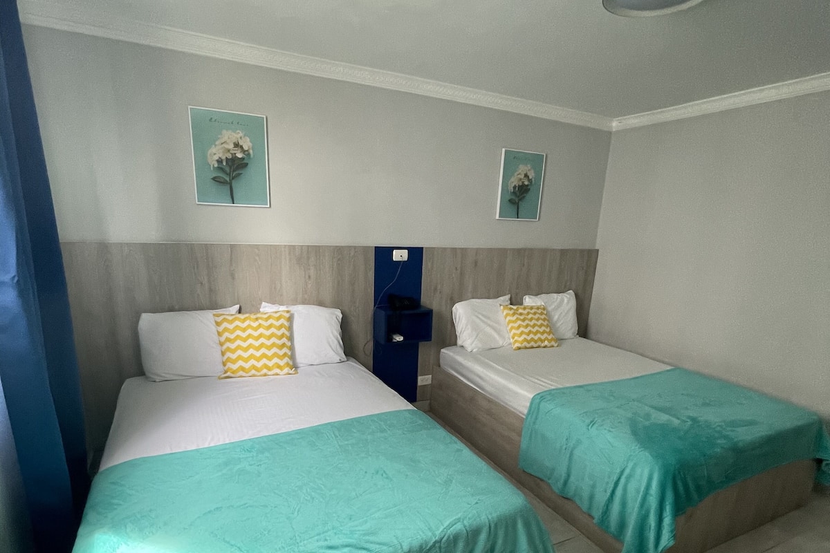 A hotel room with two single beds, a blue curtain, a wooden headboard, and a ceiling light fixture.