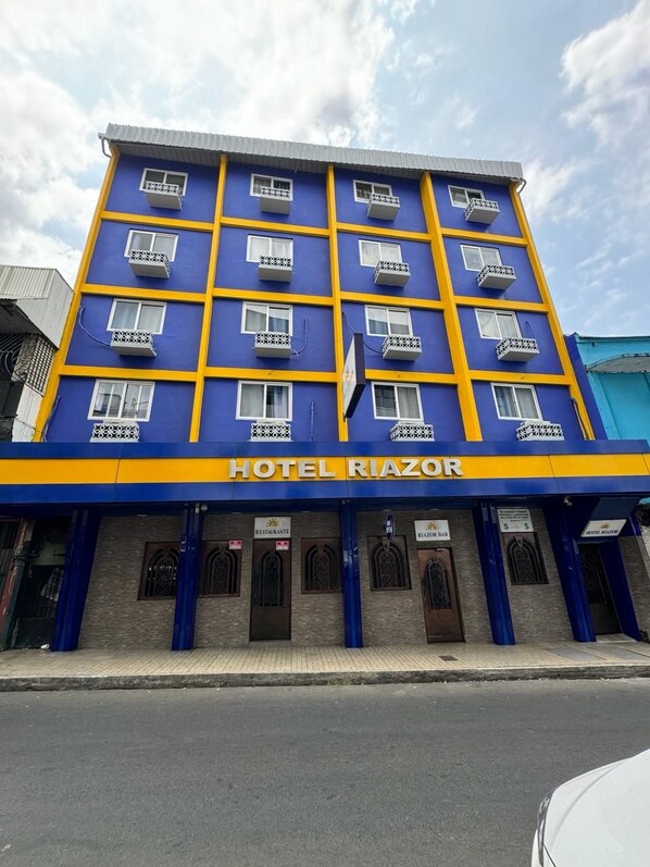 A multi-story hotel with a blue and yellow facade, named HOTEL RIAZOR.