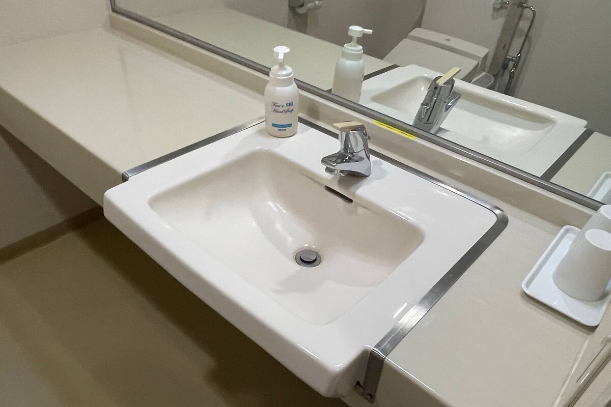 Een wit wastafeltje met een spiegel erboven, een zeepdispenser en een bekerhouder op het aanrecht.