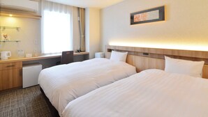 A hotel room with two beds, a desk, a chair, a small table, a mirror, and a window with curtains.
