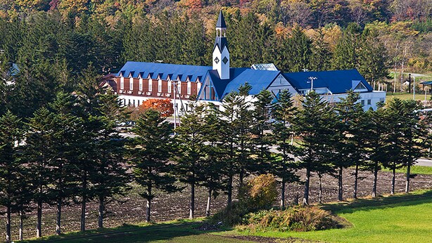 A church with a blue roof and a steeple, surrounded by trees and a field.