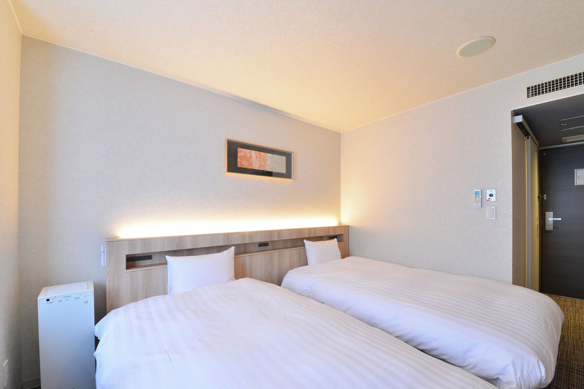 Een hotelkamer met twee bedden, een bedieningspaneel aan de muur en een deur met een codeerapparaat.