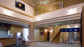 A spacious lobby with a high ceiling, a staircase connecting two floors, and a reception desk.