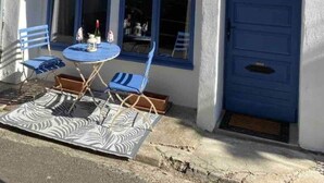 Un bâtiment avec une porte bleue, un balcon avec des chaises bleues et une table sur laquelle se trouvent une bouteille et un verre.