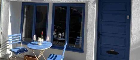 A building with a blue door, a balcony with blue chairs, and a table with a bottle and a glass.