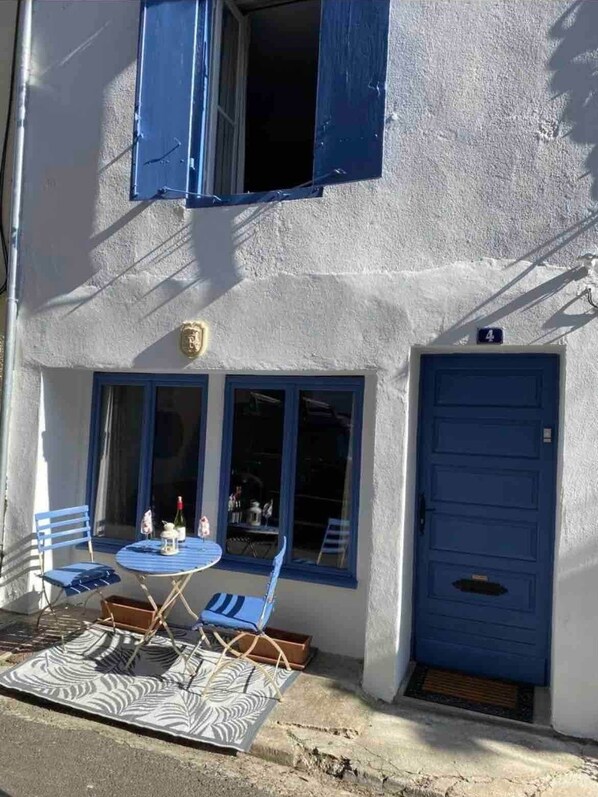 A building with a blue door, a balcony with blue chairs, and a table with a bottle and a glass. - Traditional 3 bedroom home in Quillan (Quillan)
