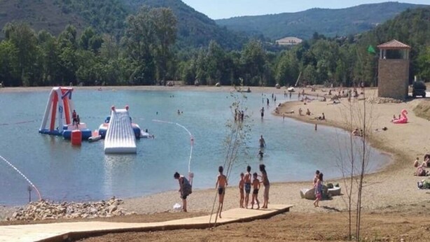 Un lac avec un petit quai, une plage et une colline en arrière-plan.