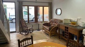 Une pièce comprenant une table à manger, un canapé, un fauteuil à bascule, un ventilateur de plafond et une vue accessible par une porte coulissante.