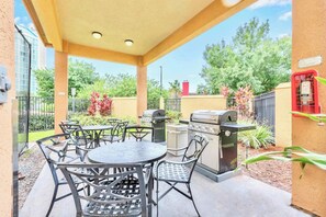 Un'area patio esterna con un tavolo rotondo e sedie, un barbecue e un cestino.