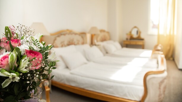 Un dormitorio con cama, mesita de noche y un jarrón de flores.