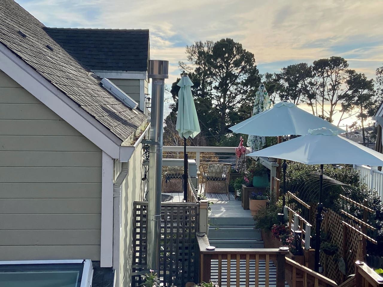 A residential backyard with a wooden deck, outdoor furniture, and a pergola with a white umbrella.