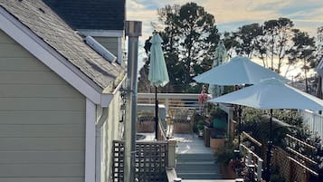A residential backyard with a wooden deck, outdoor furniture, and a pergola with a white umbrella.