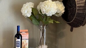 Een houten tafel met een fles Hook Creek Chardonnay, een doos Cheddar crackers en een vaas met witte bloemen.