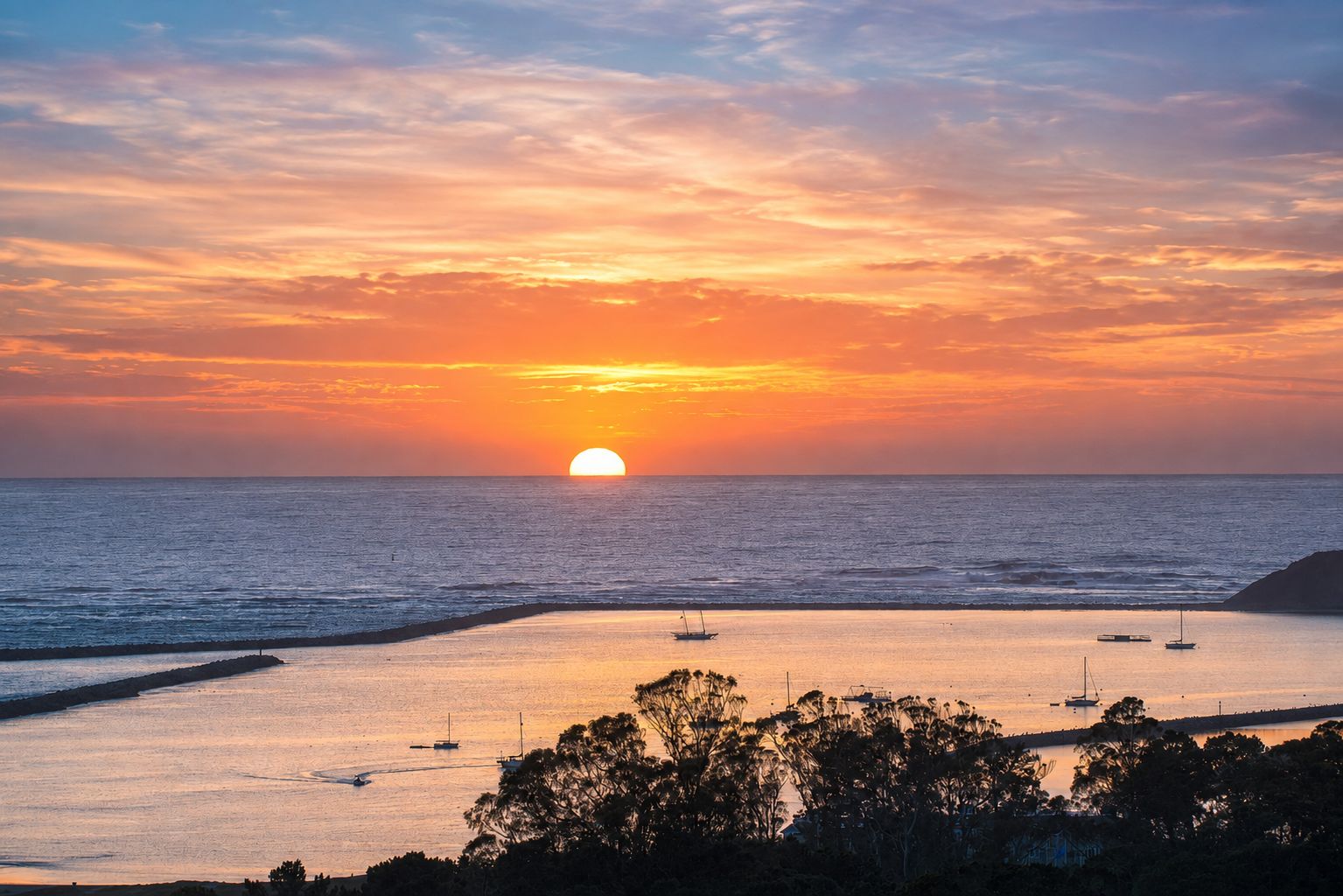 A sunset over a calm sea with boats and a beach in the foreground.