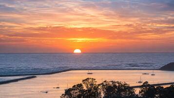 A sunset over a calm sea with boats and a beach in the foreground.