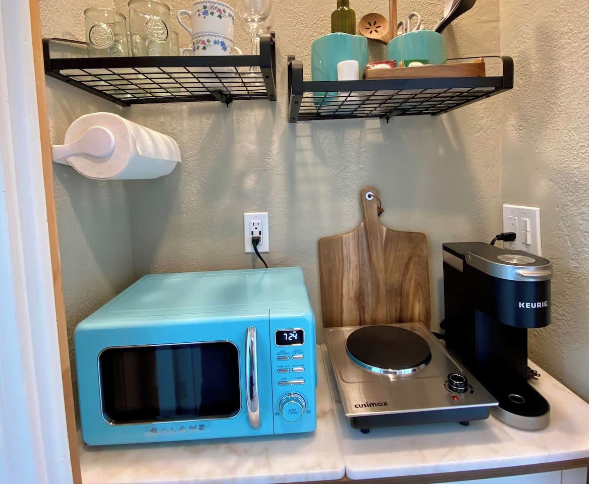A kitchen with a blue microwave, a coffee maker, and shelves with kitchenware.