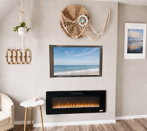 A living room with a flat-screen TV mounted above a fireplace, a wall-mounted decorative item, and a framed picture. - Oceanview Penthouse, Stylish, Walking to Beach (Half Moon Bay)