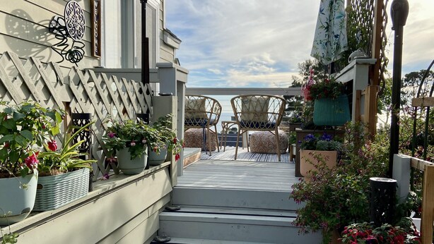 Een houten terras met een trap naar een overdekt zitgedeelte met stoelen en een tafel.