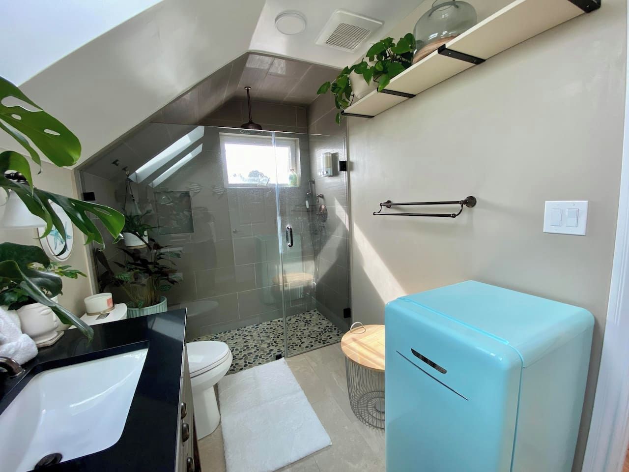 A modern bathroom with a glass-enclosed shower, a toilet, a sink, and a blue refrigerator.