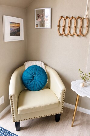 A beige armchair with a blue pillow, a small white table with a vase, and two framed pictures on the wall. - Oceanview Penthouse, Stylish, Walking to Beach (Half Moon Bay)